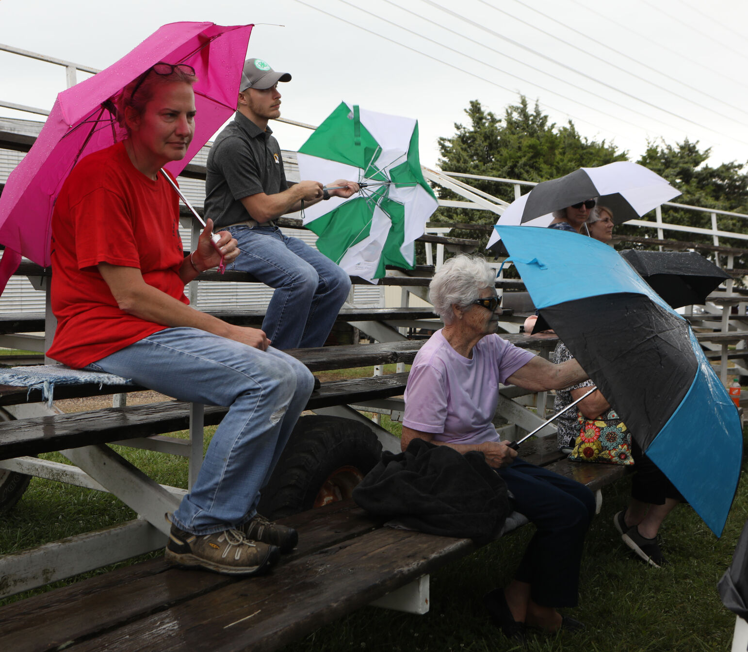 Spectators sit under umbrellas